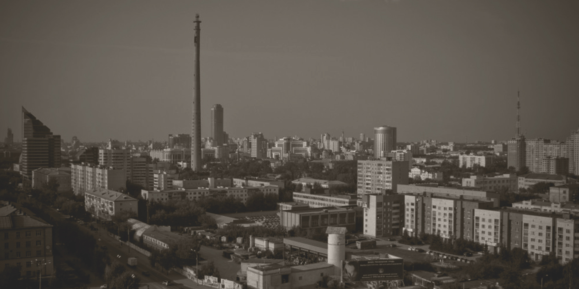 Sepia-toned wide cityscape with a tall tower, high-rise buildings, and residential blocks under an overcast sky