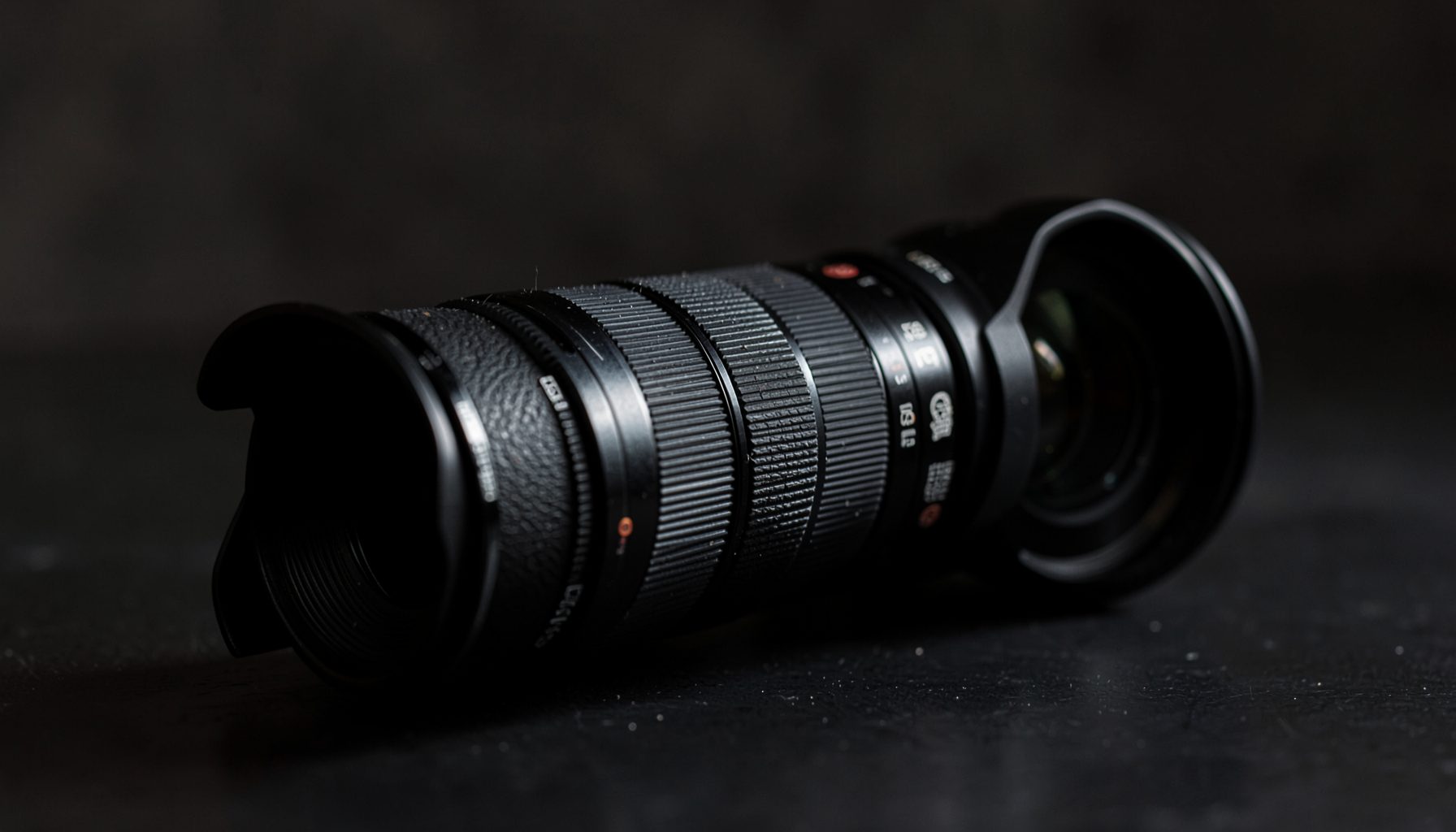 A camera with an extended lens barrel, positioned on a dark tabletop with soft directional light