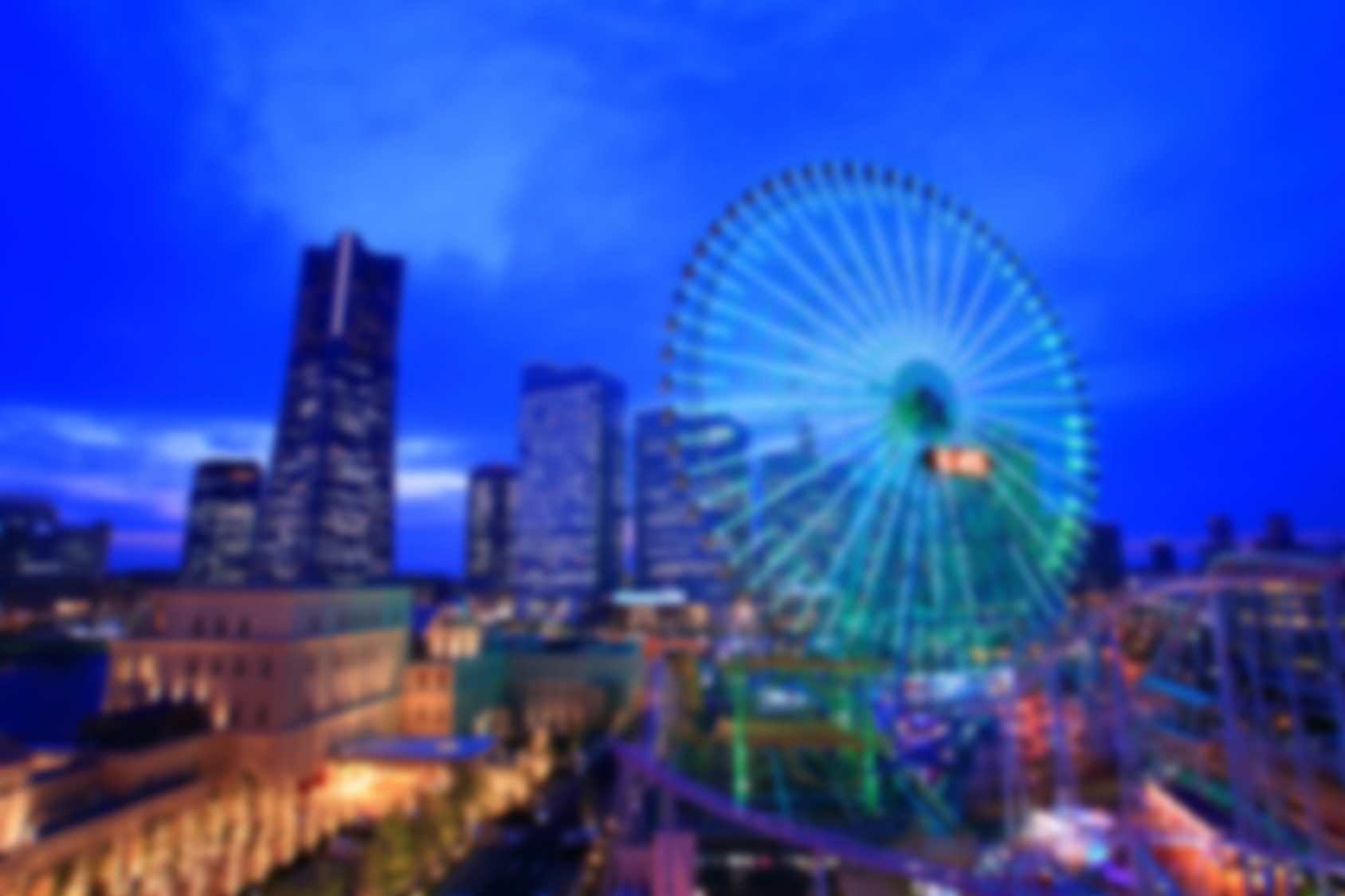 Blurred night cityscape with illuminated ferris wheel, skyscrapers, blue and green tones, dreamy mood